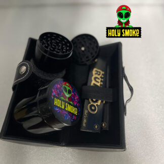 Kit de accesorios marca Holy Smoke incluye un grinder de metal negro , un contenedor y 2 papeles de fumar tamaño King